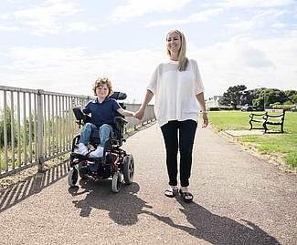 Garçon handicapé en fauteuil roulant tenant la main de sa mère sur le chemin d'accès.