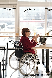 Femme en fauteuil roulant installée à une table avec une tasse à la main dans un café.