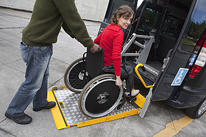 Personne se déplaçant en fauteuil roulant embarquant dans un taxi adapté.