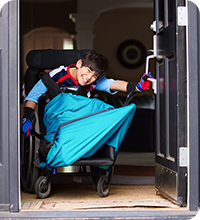 Jeune garçon souriant en fauteuil roulant qui ouvre la porte d'entrée de sa demeure.